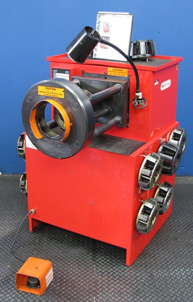 A reconditioned Aeroquip FT1390 adjustable 2 hose crimper with 12 dies, foot pedal, circular front opening, and warning labels is shown against a blue wall and black floor.