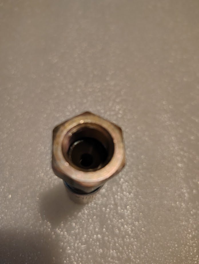 A close-up of the Weatherhead 04U-04L 1/4 Hose x 1/4 JIS Female Fitting (CS40-4X4), a metal hexagonal nut used in hydraulic hose assemblies, placed on a textured, light gray surface.