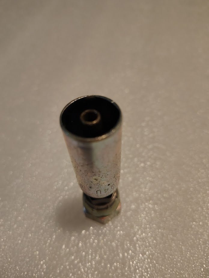 A close-up of a Weatherhead 04U-04L 1/4 Hose x 1/4 JIS Female Fitting (CS40-4X4) stands upright on a textured white surface, showing its hollow interior and threaded end.