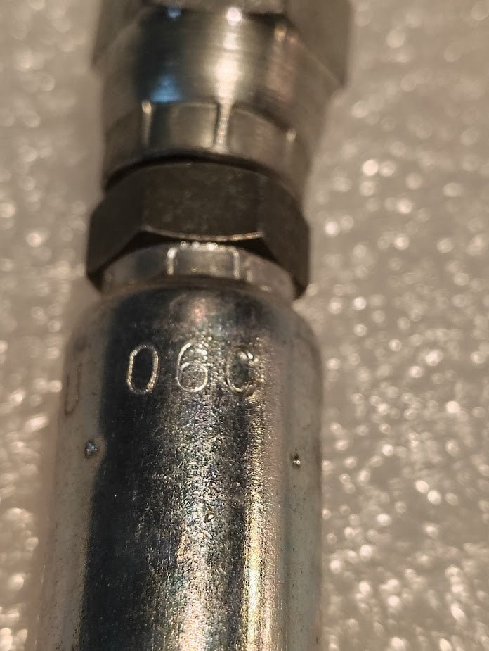 Close-up of a Weatherhead 04U-06C 1/4 Hose x M12x1.5 DIN Female Fitting (CS37-4X6), with 060 engraved, resting on textured white bubble wrap.