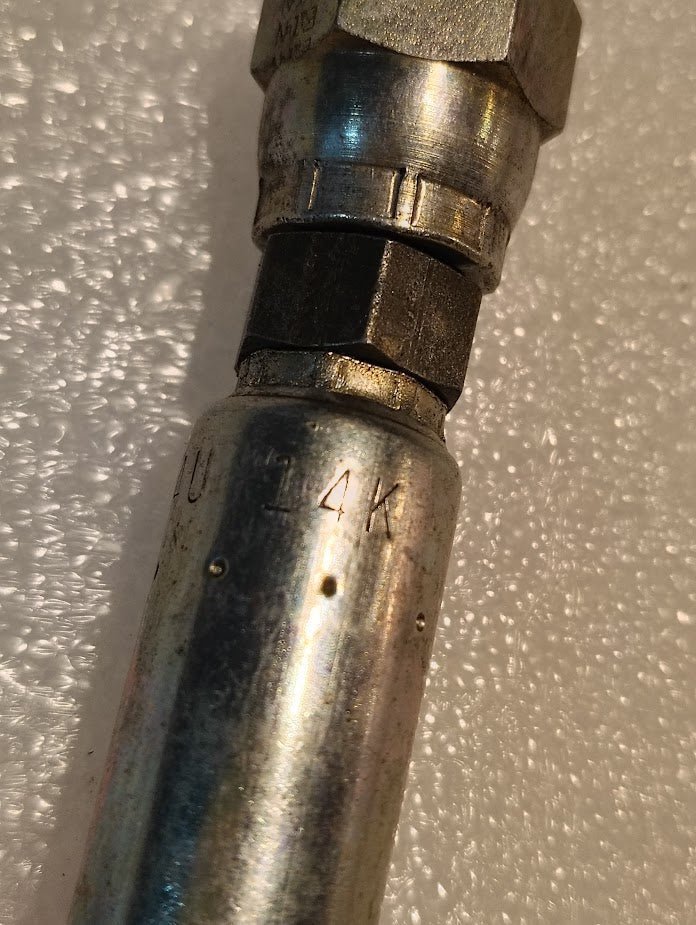 Close-up of a Weatherhead 04U-14K hydraulic hose fitting (1/4 x M14x1.5 Komatsu female, CS39-4X14) on a textured white surface.