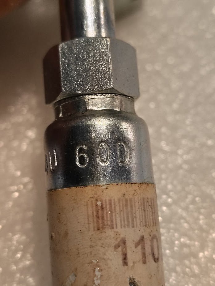 Close-up of Weatherhead 04U-60D, a 1/4 hose x M16x1.5 DIN female fitting (CS44-4X10), attached to a white cylindrical item showing part of a barcode and the number 110. The metal fitting is stamped with 60D.