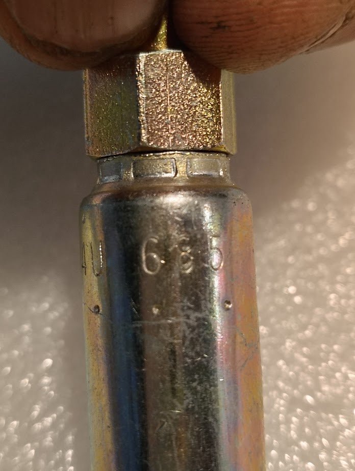 A close-up shows a Weatherhead 04U-685 1/4 Hose x 5/16 JIC/SAE Female Fitting (CS25-4X5) held by hand, with engraved markings visible; the background is blurred.