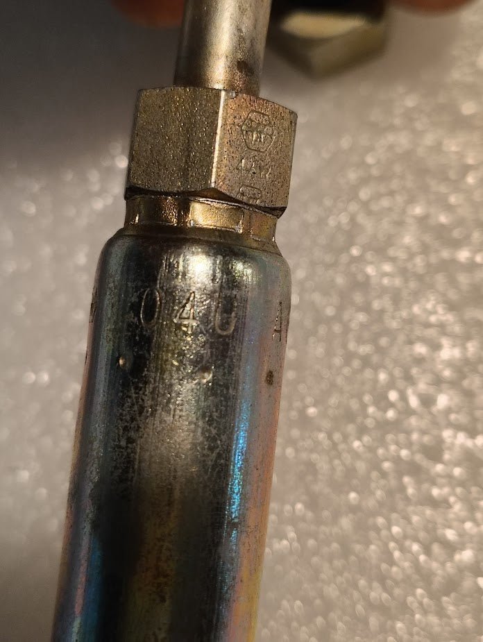 Close-up of a Weatherhead 04U-A64 1/4 Hose x 1/4 ORF Female Fitting (CS33-4X4) showing metallic surface with stamped markings 040 and A, set against a textured, light-colored background.