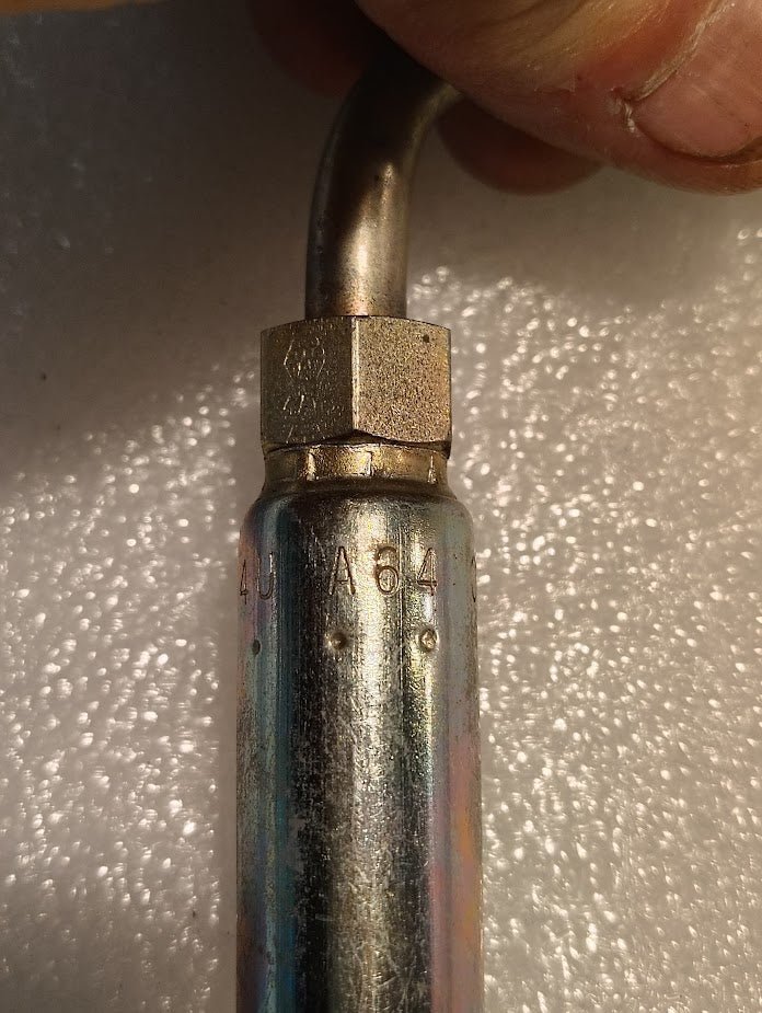 Close-up of the Weatherhead 04U-A64, a metallic pipe with a hexagonal nut on top, bearing 430 and 433 engravings. Its held by hand at its curved end against a textured white surface, showcasing the precision and sleek design of this 1/4 hose x 1/4 ORF female fitting - 90 long swivel.