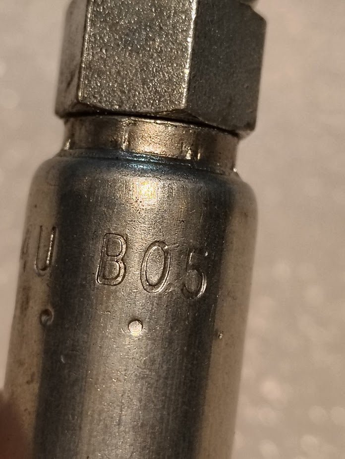 Close-up of a Weatherhead 04U-B05, 1/4 hose x 5/16 inverted male fitting (CS18-4X5), metallic and cylindrical with B05 markings and threaded hexagonal top. Surface shows wear; background is blurred.