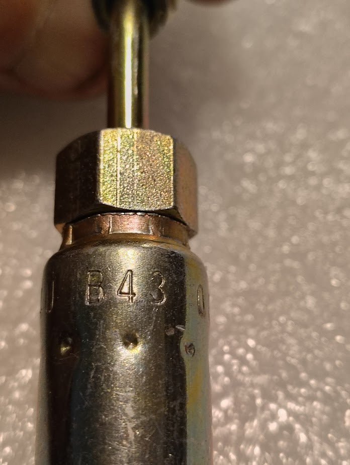 Close-up of the Weatherhead 04U-B43 (1/4 hose x 3/16 inverted male fitting, CS19-4X3), showing its threaded fitting and hex nut—commonly used for hydraulic hoses—held in a hand against a textured background.