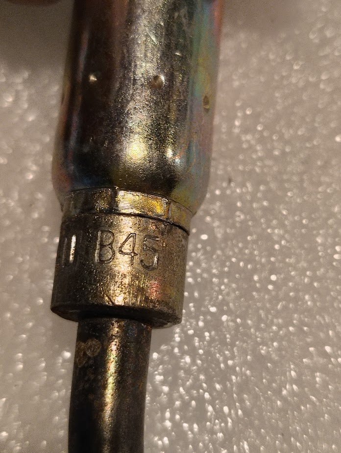 Close-up of the 04U-B45, a Weatherhead 1/4 Hose x 5/16 Inverted Male Fitting (CS19-4X5), attached to a black cable and resting on a textured white foam surface.
