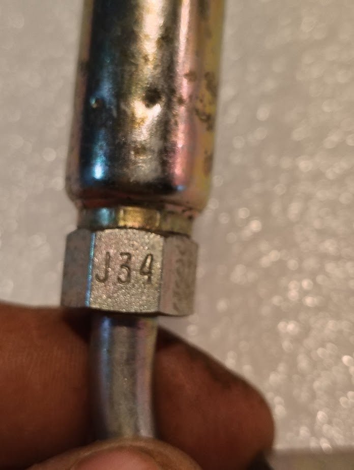 A close-up shows the Weatherhead 04U-J34, a 1/4 hose x 1/4 ORF female fitting (CS34-4X4), with J34 engraved on its hexagonal nut, held by fingers against a blurred, textured background highlighting hydraulic hose fittings.