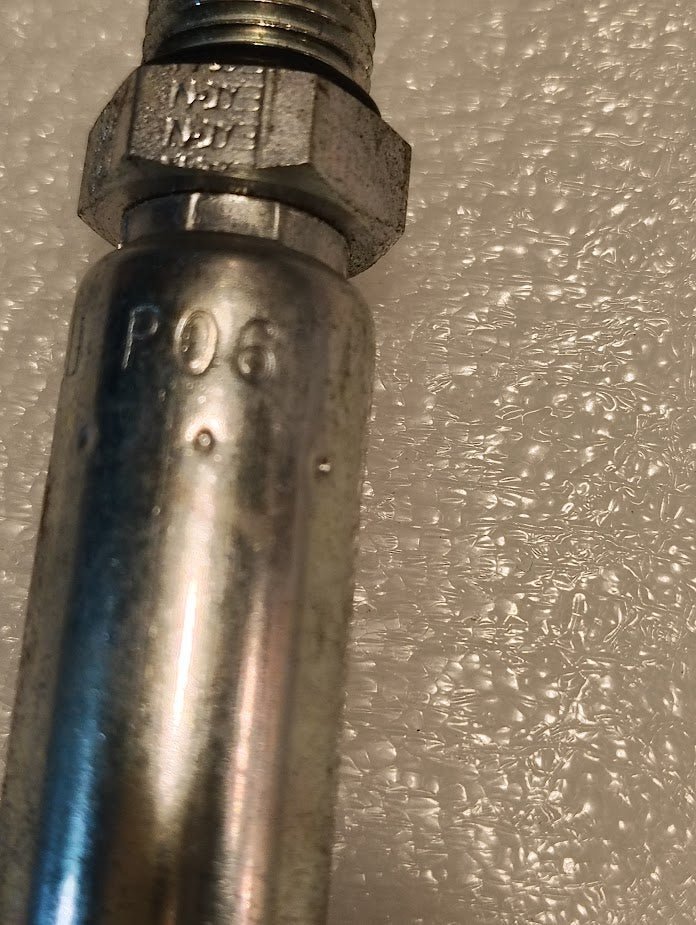 A close-up of a metallic, threaded 04U-P06 | Weatherhead 1/4 Hose x 3/8 ORB Male Fitting (CS11-4X6), engraved with code P06 and placed on bubble wrap, used for reliable hydraulic hose connections.