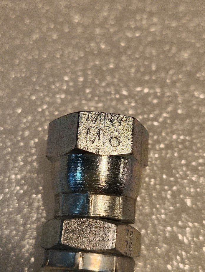 A close-up of the Weatherhead 06U-10C CS37-6X10, a 3/8 hose x M16x1.5 DIN female fitting, shown on a textured, light background—ideal for compatible hydraulic hose applications.