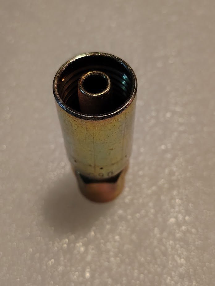 A close-up of the 06U-204 Weatherhead fitting reveals a brass and copper cylinder with a threaded interior, designed for 3/8 hose x 1/4 NPTF connections. The shiny surface reflects light beautifully against a softly blurred white background.