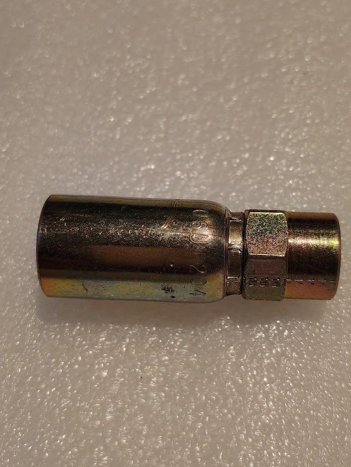 The Weatherhead 06U-204 fitting, a metallic hydraulic hose adapter with a threaded end, lies horizontally on a textured white surface. Its cylindrical design is compatible with 100R1 hoses for secure connections.