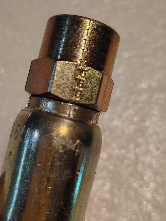 A close-up of a Weatherhead 06U-204 fitting on a light backdrop reveals its metallic appearance, threading, hexagonal middle, and engraved markings typical of 100R1 hoses. The fitting shows signs of wear.