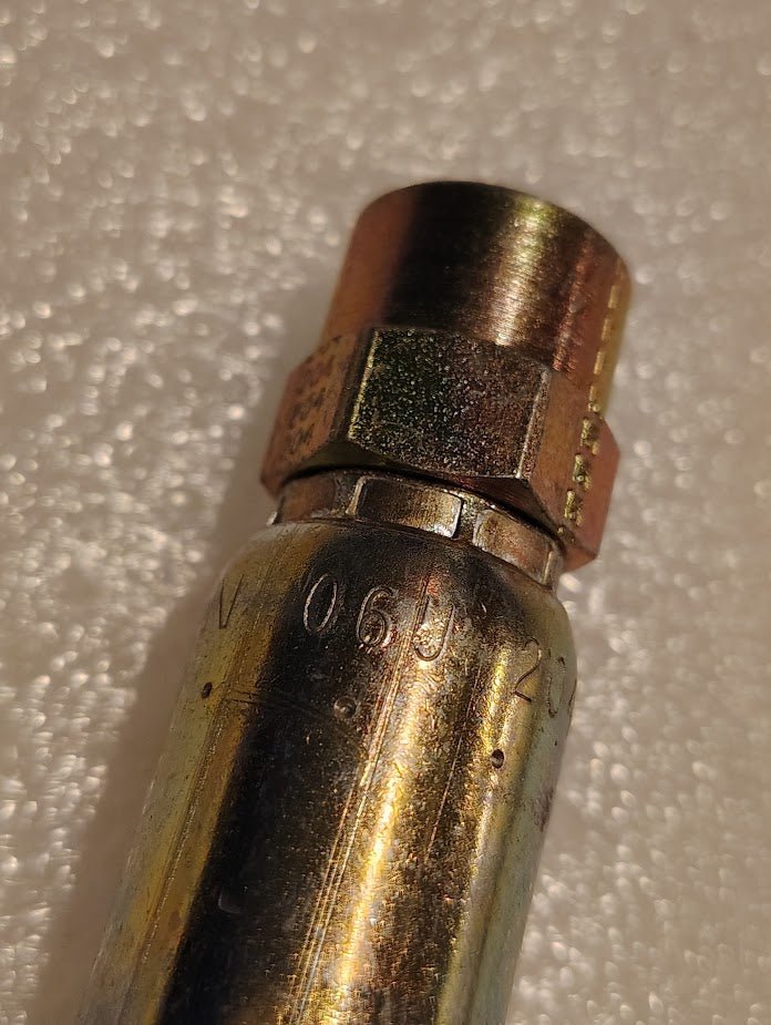 The 06U-204 Weatherhead fitting, designed for 3/8 hoses and 1/4 NPTF connections, features a hexagonal brass and metallic design with engraved markings on a textured white backdrop, showcasing precision engineering for hydraulic systems like the 100R1 hoses.