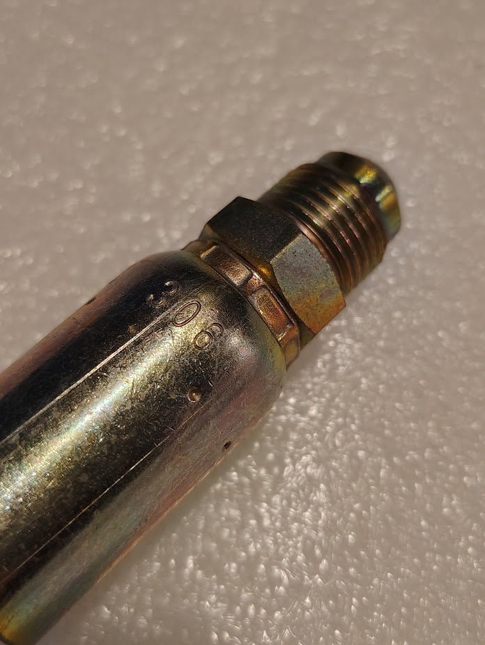 A close-up of the Weatherhead 06U-306 3/8 Hose x 3/8 SAE Male Fitting (CS06-6X6) on a textured, light surface; its hexagonal nut and shiny metal show slight tarnish and visible stamped markings typical for hydraulic fittings.
