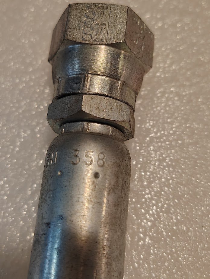 Close-up of a Weatherhead 06U-358 (3/8 Hose x 1/2 BSPP Female Fitting, CS10-6X8) metallic fitting with hexagonal nuts and markings 358 and 21, featuring hydraulic hose fittings against a textured white background.
