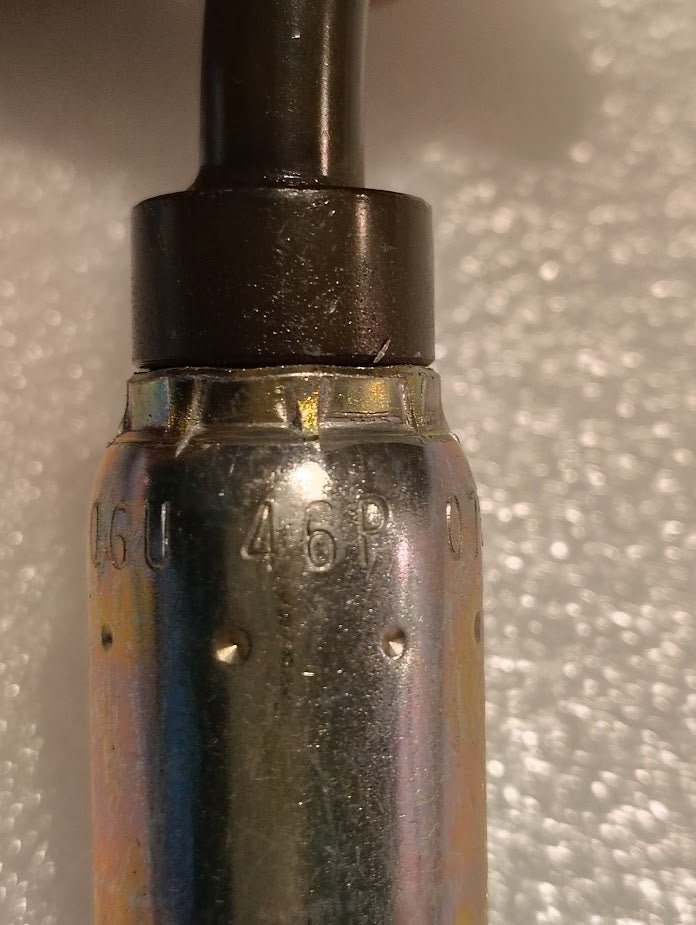 Close-up of a Weatherhead 06U-46P (3/8 Hose x 3/8 BSPP Female Fitting, CS43-6X6) with engraved numbers attached to a black cable on a textured white background—compatible with 100R1 hydraulic hose fittings.