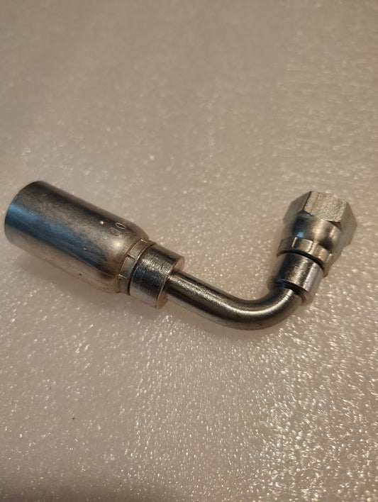 The 06U-60D Weatherhead 3/8 Hose x M16x1.5 DIN Female Fitting (CS44-6X10) features an angled, elbow-shaped metal design with a hex nut on one end, shown resting on a textured white surface.