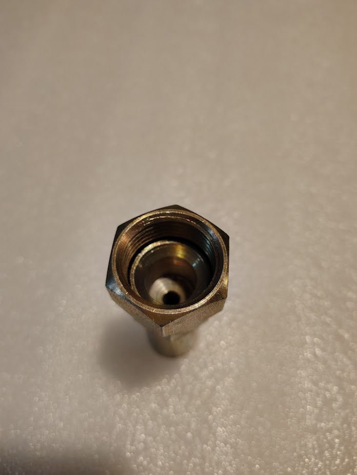 A metallic hexagonal nut with an open center, similar to the Weatherhead 3/8 Hose x 3/4 JIC Female Fitting - Straight Swivel (06U-612), shines brightly on a textured white surface.