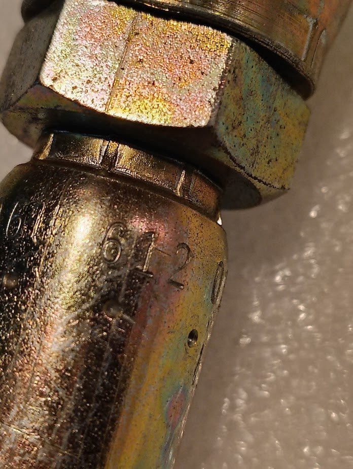 Close-up of the Weatherhead 3/8 Hose x 3/4 JIC Female Fitting (06U-612, CS09-6X12)—a metallic, rainbow-tinted connector engraved with 6120 and compatible with Parker fittings—on a light, textured surface.