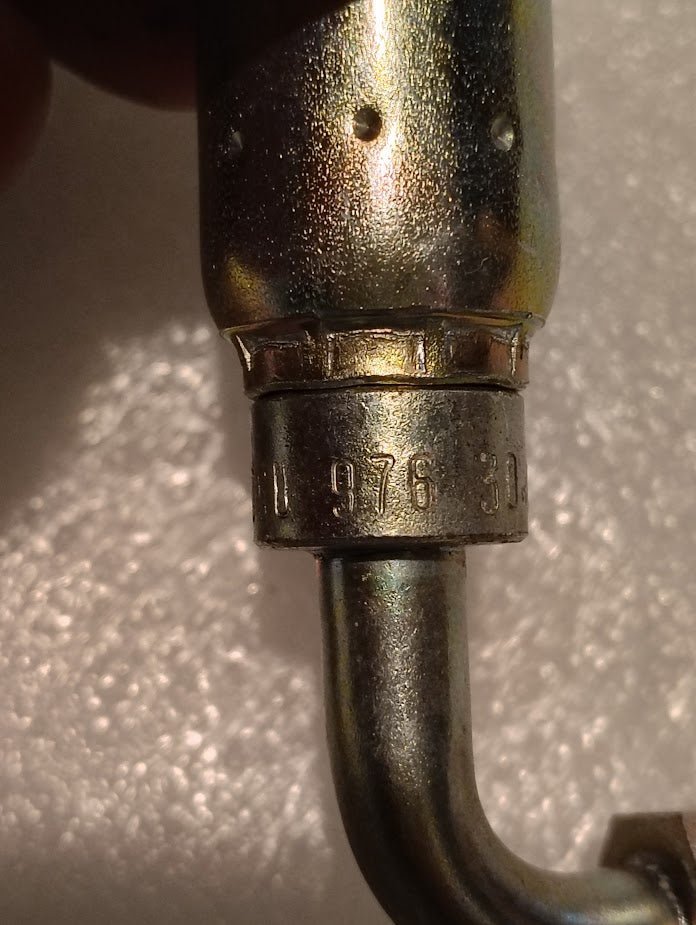Close-up of a 06U-976 Weatherhead 3/8 Hose x 3/8 Flareless Fitting with a 90° bend, showing the curvature and partial engraving 976 3 on the ring, set against a textured white background.