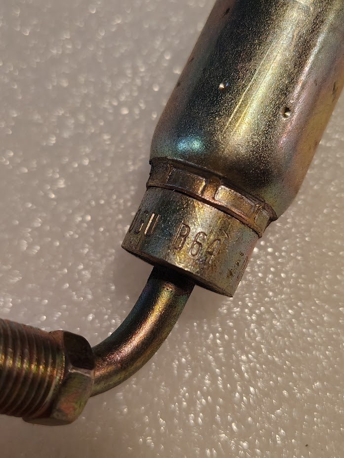 Close-up of a metallic 06U-B64 Weatherhead 3/8 Hose x 1/4 Inverted Male Fitting (CS20-6X4) with B64 markings on the metal surface, resting on a textured white background.