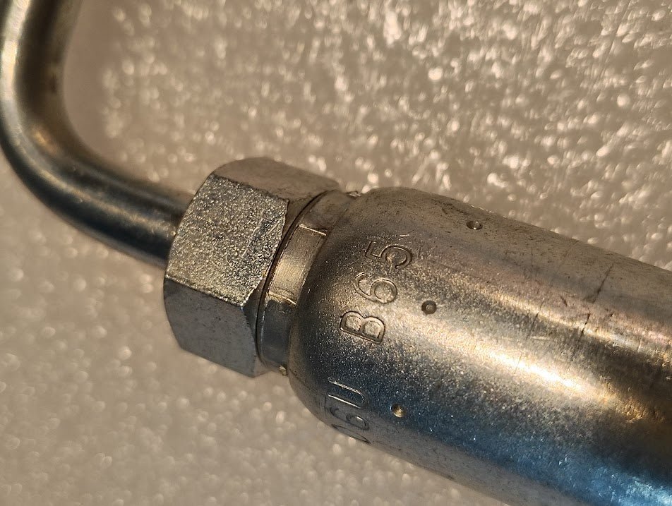 Close-up of the 06U-B65 Weatherhead 3/8 Hose x 5/16 Inverted Male Fitting (CS20-6X5), featuring a hex nut engraved with B65 and 16U, commonly used in hydraulic hose assemblies, against a textured white background.