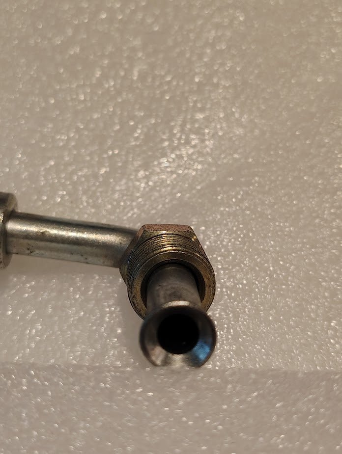 Close-up of a 06U-B67 Weatherhead 3/8 Hose x 7/16 Inverted Male Fitting (CS20-6X7) with a threaded hexagonal nut, angled to display its open end against a textured white background.