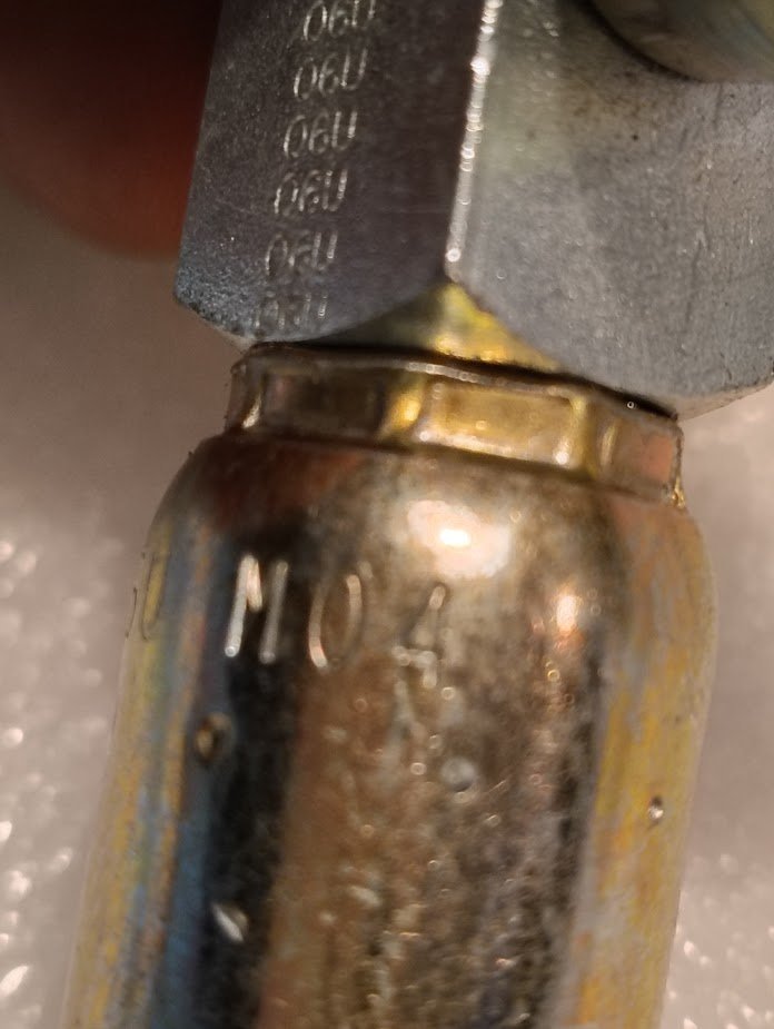Close-up of a Weatherhead 06U-M04 fitting (3/8 hose x 1/4 NPTF male, CS14-4X6), showing engraved markings and a hexagonal nut joined to a cylindrical, slightly worn metallic surface.