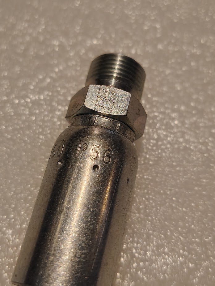 A close-up photo of a 06U-P56 Weatherhead 3/8 Hose x 3/8 BSPT Male Fitting (CS36-6X6), showing its metallic threads and engraved P56 markings, lying on a textured, light-colored surface.