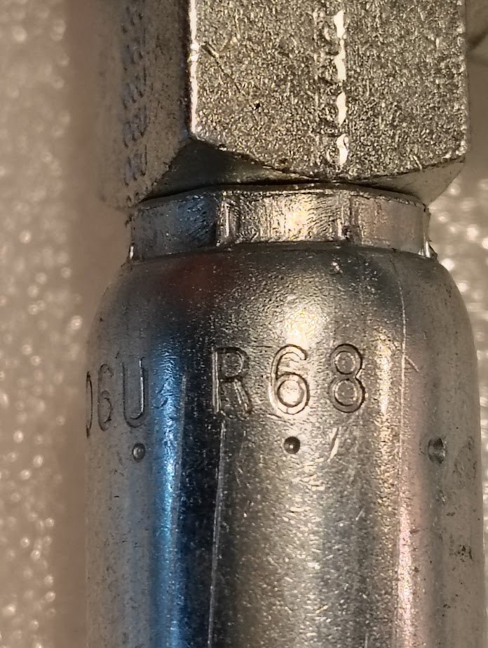 Close-up of the Weatherhead 06U-R68 CS15-6X8, a 3/8 hose x 1/2 ORB male fitting with engraved markings, shown against a textured light background—ideal for compatible fittings and hydraulic hose systems.