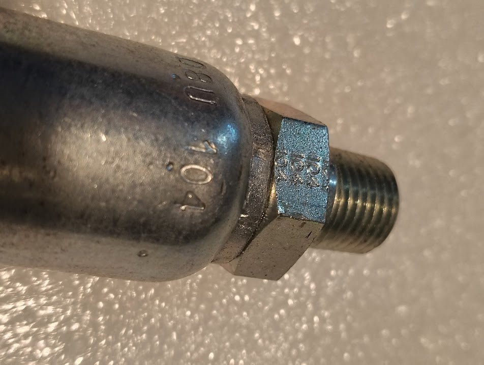 Close-up of a Weatherhead 08U-104 (1/2 Hose x 1/4 NPTF Male Fitting, CS01-8X4) metal pipe fitting with engraved markings, typically used for hydraulic hoses, shown against a textured light background.