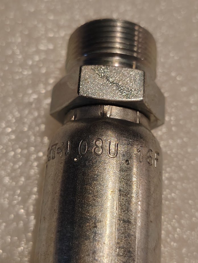 Close-up of a Weatherhead 08U-16F fitting (1/2 hose x M24x1.5 DIN male, CS67-8X16) with engraved markings and hex nut on a white textured surface; ideal for use with compatible hoses.