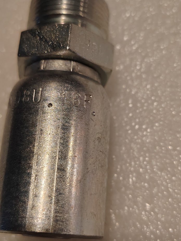 A close-up of the metallic Weatherhead 08U-16F fitting reveals engraved markings. Its reflective, slightly worn surface suggests 100R1 compatibility, set against a textured white background.