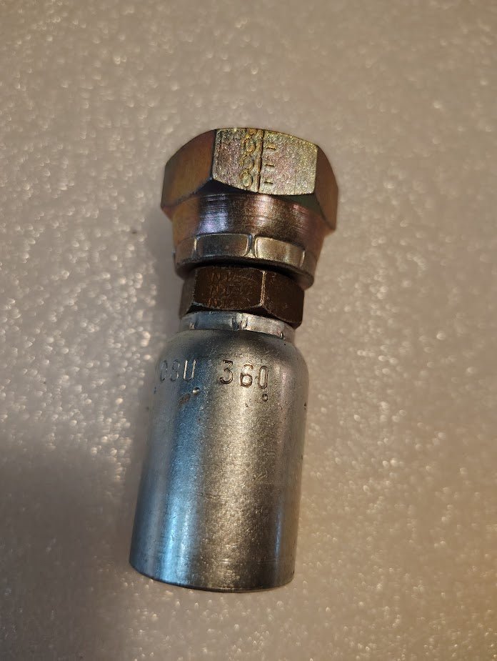 A close-up of the Weatherhead 08U-360, a 1/2 hose x 5/8 BSPP female hydraulic fitting with hex nut and crimped end on white textured surface—ideal for demanding hydraulic applications with 100R series hoses.