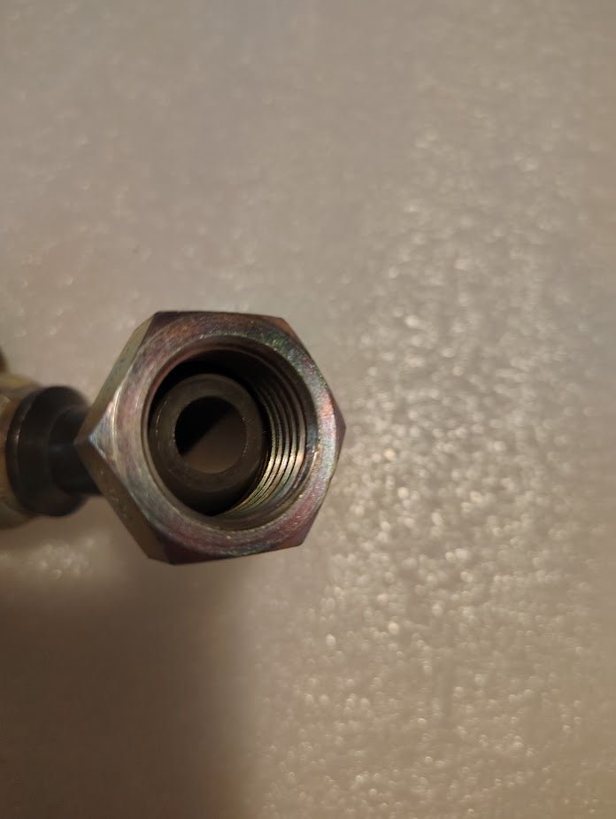 Close-up of the Weatherhead 08U-48P 1/2 Hose x 1/2 BSPP Female Fitting (CS43-8X8), showing its metallic hexagonal nut and internal threading, attached to a pipe on a light, textured surface.