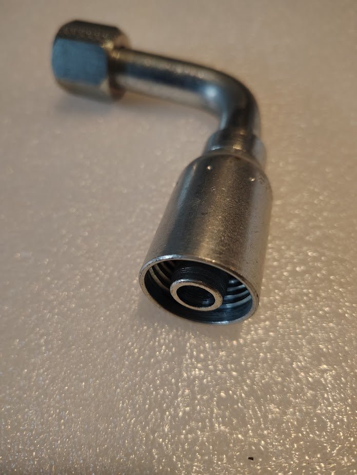 A close-up of the 08U-650 Weatherhead 1/2 Hose x 5/8 JIC/SAE Female Fitting (CS27-8X10) with a 90-degree bend rests on a textured white surface, showing the threaded opening facing the camera. Suitable for Weatherhead fittings and 100R2 hoses.