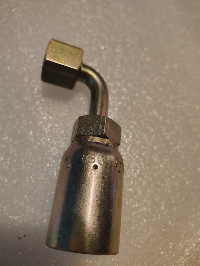 The Weatherhead 08U-A26 is a 1/2 hose x 3/8 ORF female fitting. It features an L-shaped elbow with threaded connections, showcased against a textured white background. A hexagonal nut at one end ensures secure attachment.
