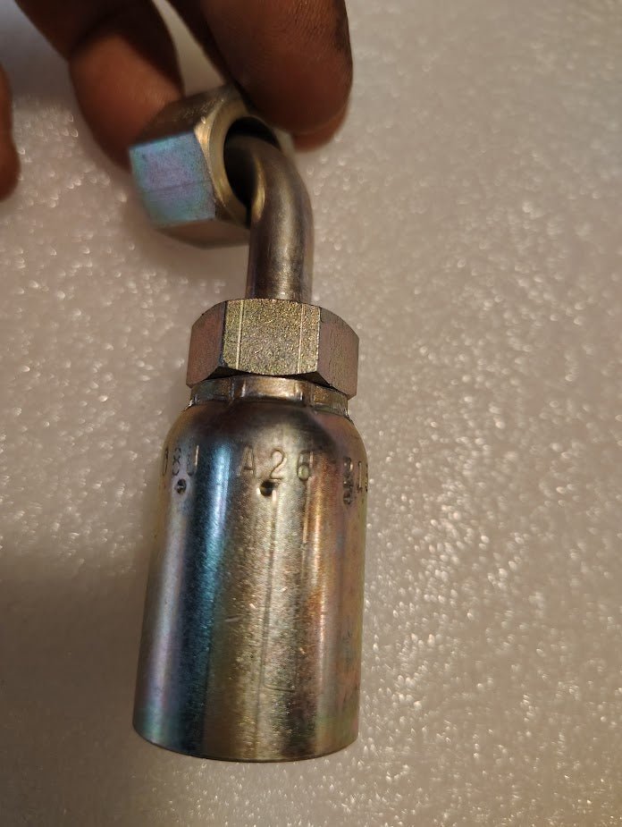 A hand holds the Weatherhead 08U-A26 (1/2 Hose x 3/8 ORF Female Fitting, CS32-8X6), a metallic hydraulic connector ideal for 100R1 hoses, against a textured white background.