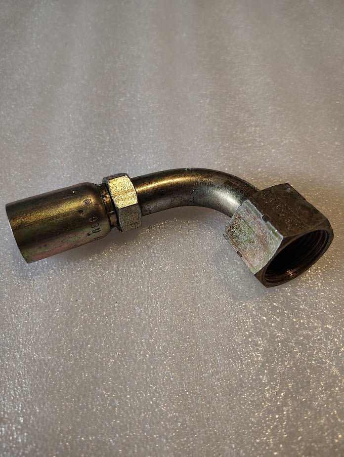 The 08U-A32 Weatherhead 1/2 Hose x 3/4 ORF Female Fitting (CS32-8X12), a metal hydraulic fitting with a 90-degree bend, is shown on a textured, light surface. It’s made for use with 100R1 hoses and features a threaded hex nut.