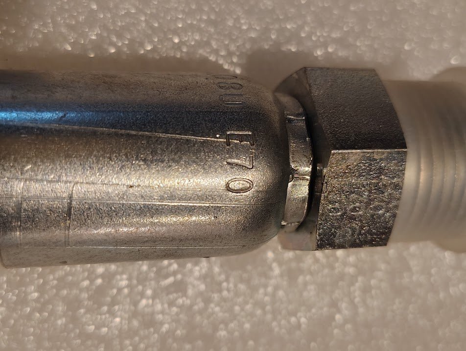 Close-up of a Weatherhead 08U-E70 (CS29-8X10) 1/2 hose x 5/8 ORF male fitting with hexagonal nut and engraved markings, commonly used in hydraulic systems, displayed on a white textured surface.