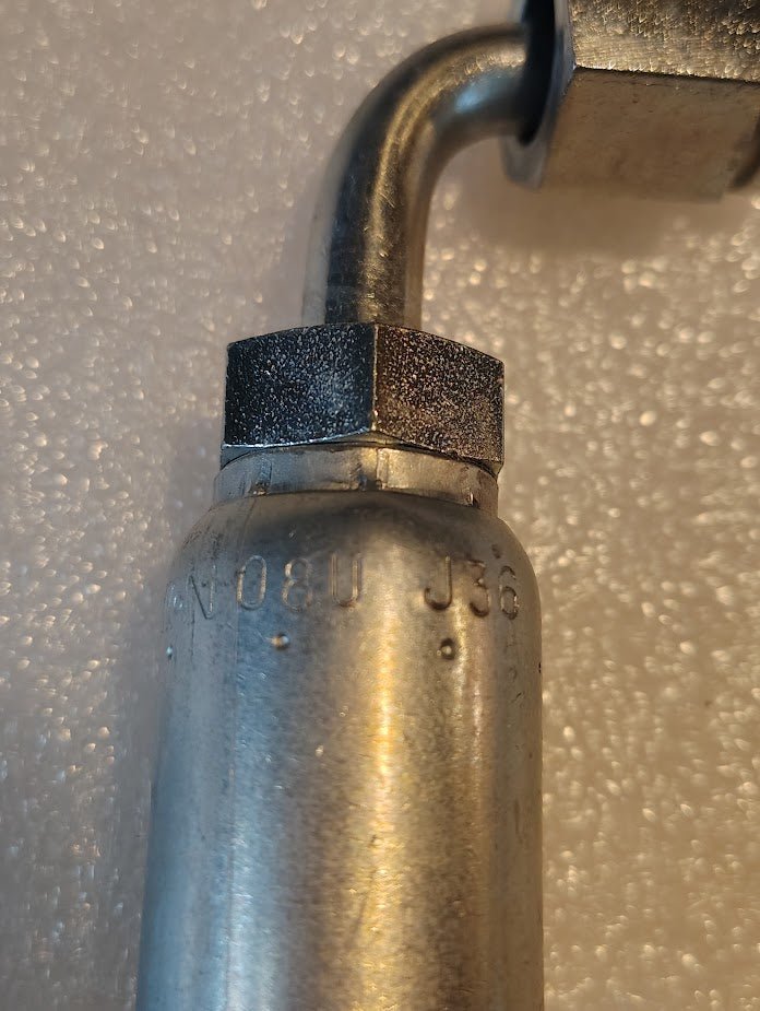 A close-up of a Weatherhead 08U-J36 fitting, a 1/2 hose x 3/8 ORF female connector (CS34-8X6), with curved metal pipe, hexagonal nut, and engraved markings on a textured white surface.