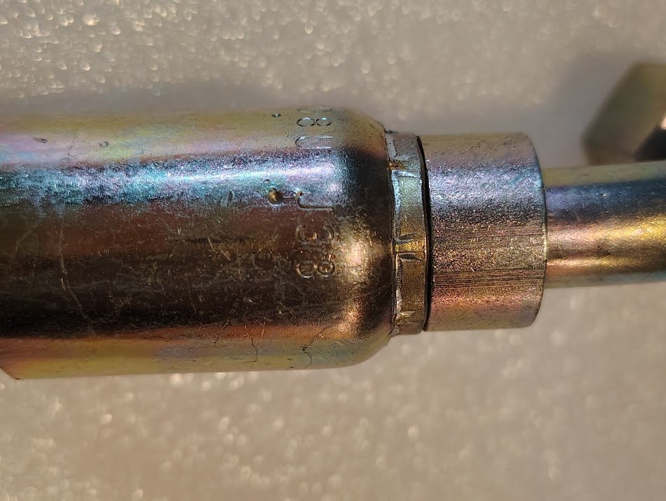 Close-up of a Weatherhead 08U-J38 1/2 Hose x 1/2 ORF Female Fitting (CS34-8X8), metallic and cylindrical with a threaded joint, showing scratches and stamped numbers, set against a textured white background.