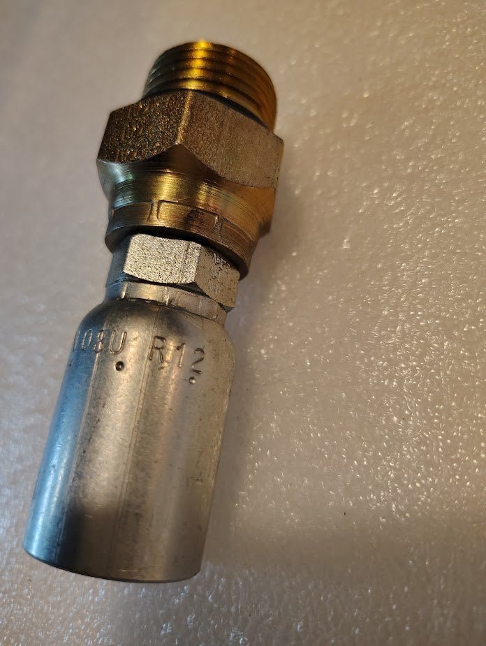 A close-up of the 08U-R12 | Weatherhead 1/2 Hose x 3/4 ORB Male Fitting with brass threads and engraved markings, compatible with Weatherhead fittings, shown on a textured white surface.