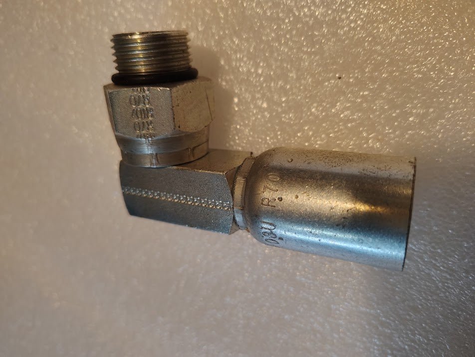 A close-up of the 08U-R70 Weatherhead 1/2 Hose x 5/8 ORB Male Fitting (CS15-8X10), featuring a threaded male end and crimped hose connector, resting on a textured white surface.