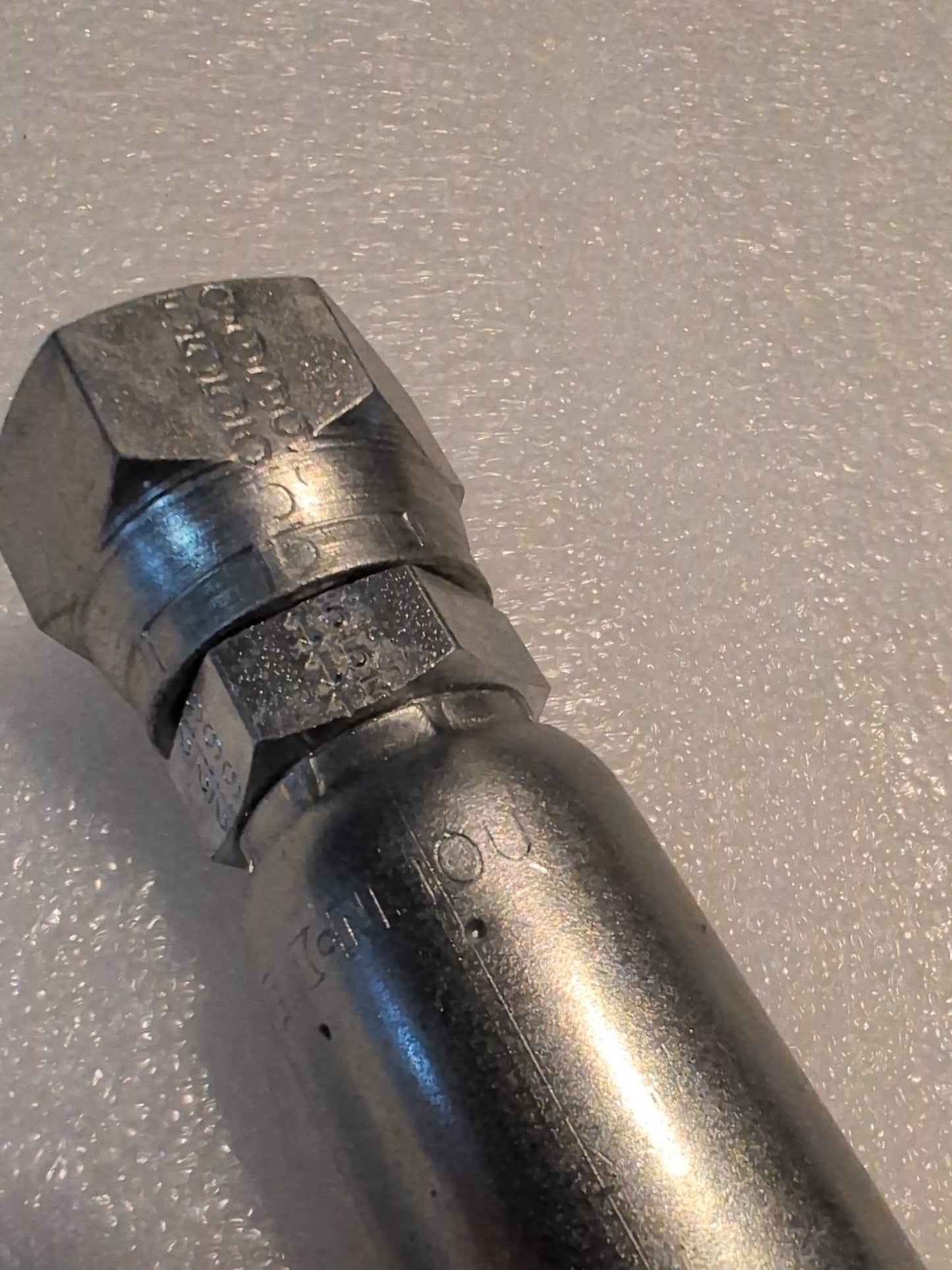 Close-up of a hexagonal bolt with engraved markings, compatible with the Weatherhead 10U-612 fitting. The shiny metallic bolt rests on a textured white surface.