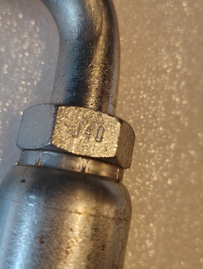 Close-up of a 10U-J40 Weatherhead 5/8 Hose x 5/8 ORF Female Fitting (CS34-10X10), featuring a hexagonal nut, often used with hydraulic hose fittings, set against a textured white background.