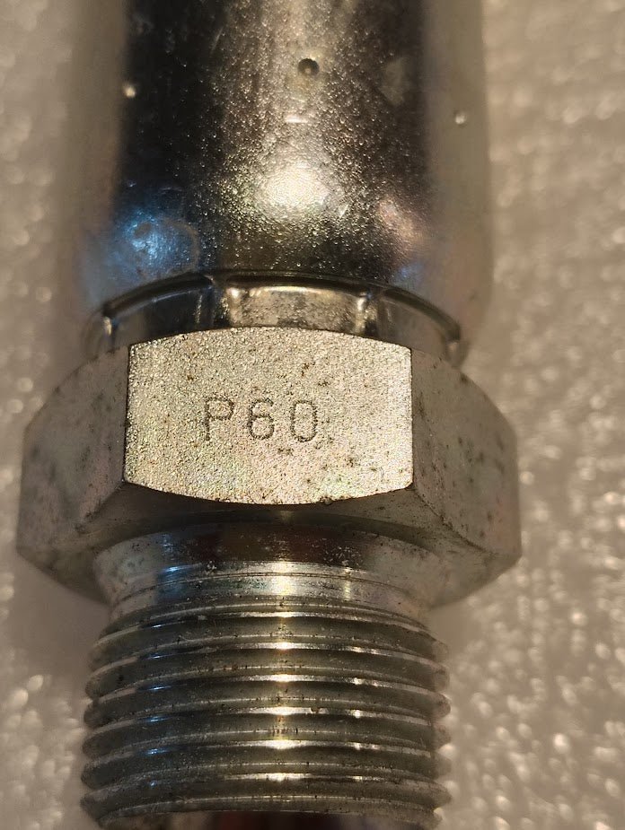 A close-up of a 10U-P60 Weatherhead CS36-10X10, 5/8 Hose x 5/8 BSPT Male Fitting, with a metallic hexagonal nut engraved P60; the textured, blurred background highlights its hose compatibility.