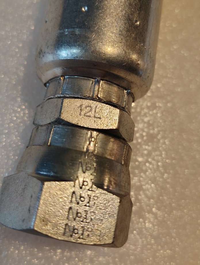 Close-up of the Weatherhead 12U-12L (CS40-12X12) 3/4 hose x 3/4 JIS female metal hydraulic fitting, with engraved numbers, on a textured, light surface—ideal for compatible fittings and hydraulic hose setups.